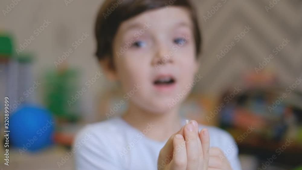 A little boy stands in a children's room and shakes his fingers a milk tooth. The boy pulls a milk tooth out of his mouth and is surprised. A little boy stands in a children's room and shakes his fingers a milk tooth. The boy pulls a milk tooth out of his mouth and is surprised.
