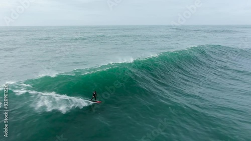 sportsman surfs ocean wave with heavy foam following scooter photo