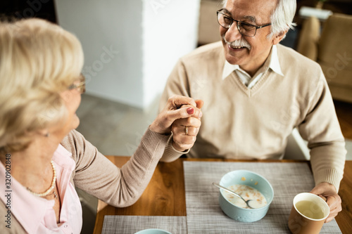 Happy mature couple holding hands at dining table.