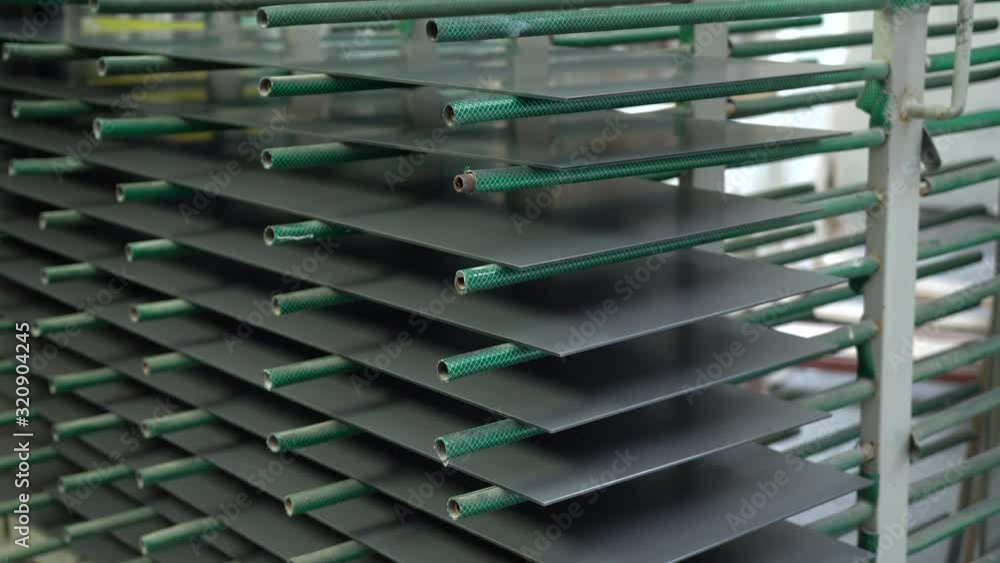 Painted glass sheets are drying on the metal carrier in warehouse. Glass factory stock. Gray painted glass panels on the green shelves. Painted glass sheets are drying on the metal carrier in warehouse. Glass factory stock. Gray painted glass panels on the green shelves.