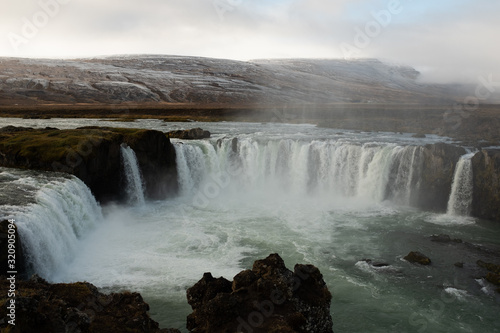 misty waterfall with snow covered mountains in the background