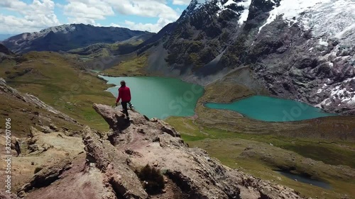 Aerial, drone shot around a womanwalking to the top of a cliff, in front of the Ausangate Glacier mountain, on a sunny day, in the Andes, Peru, South America photo