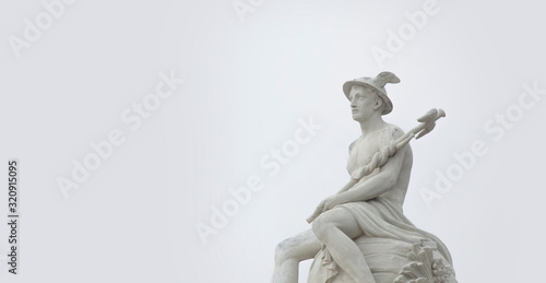 Ancient statue of god of commerce, merchants and travelers Hermes (Mercury) against gray background. He is olympic gods messenger with wings on his feet and helmet.