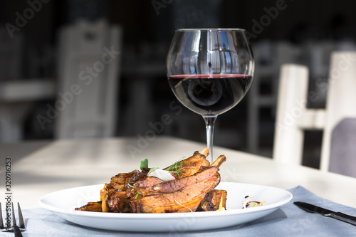 Ribs in honey onion glaze on a white plate with a glass of red wine