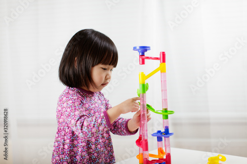 toddler girl play marble run game at gome agianst white background photo