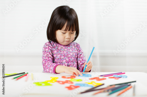 toddler girl practice writing letters on white paper against white background