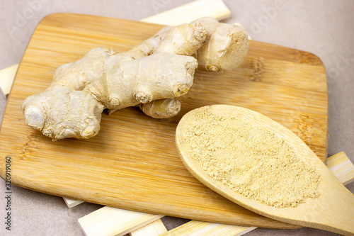 Fresh raw yellow ginger root with ground dry powder in wooden spoon and on wood background.
