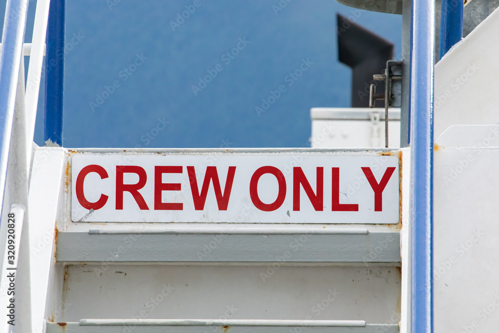 Red lettered signboard on white background saying Crew Only. Warning sign on the command bridge of a passenger ferry navigating in a canadian lake.