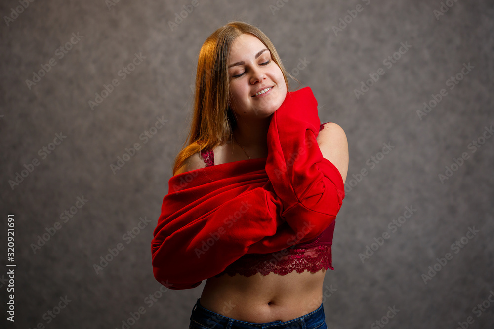 Girl tries on a red sweater on a gray background