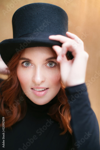 A red-haired girl in a black magicianÕs top hat looks at the camera and smiles mysteriously.