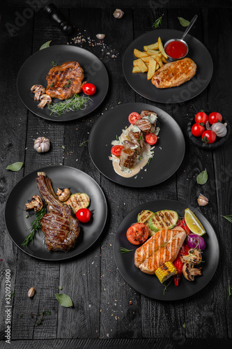 Plates with dishes: beef steak on a bone, grilled salmon fillet, skewers in a creamy sauce, pork steak, grilled chicken fillet with sauce. Octoberfest party dinner. Festive table with delicious food