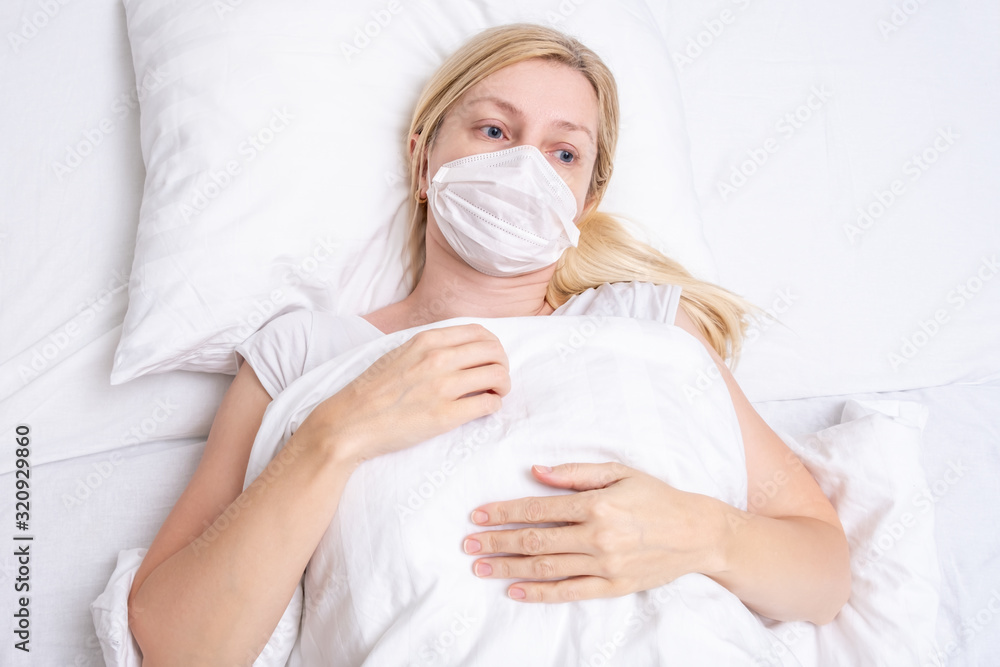 Caucasian adult woman lying in bed with flu, cold and fever, she is sick and wearing face mask