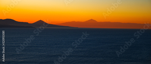 Spectacular sky colors and sunset landscape of a volcanic island with sun reflections in calm ocean.