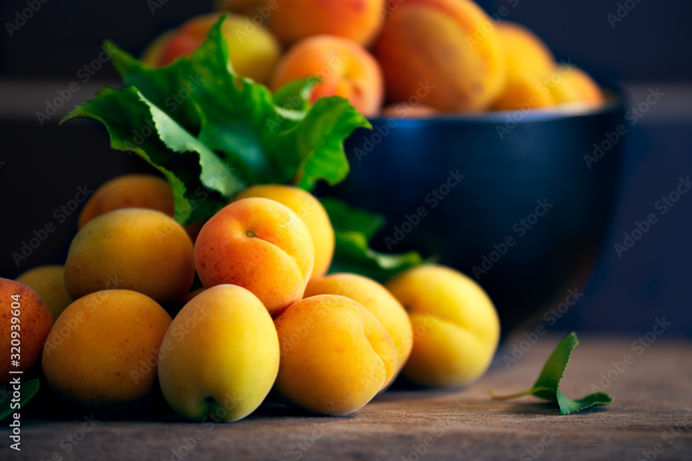 Close up of overflowing bowl of organic apricots and leaves on rustic wooden chopping block Close up of overflowing bowl of organic apricots and leaves on rustic wooden chopping block