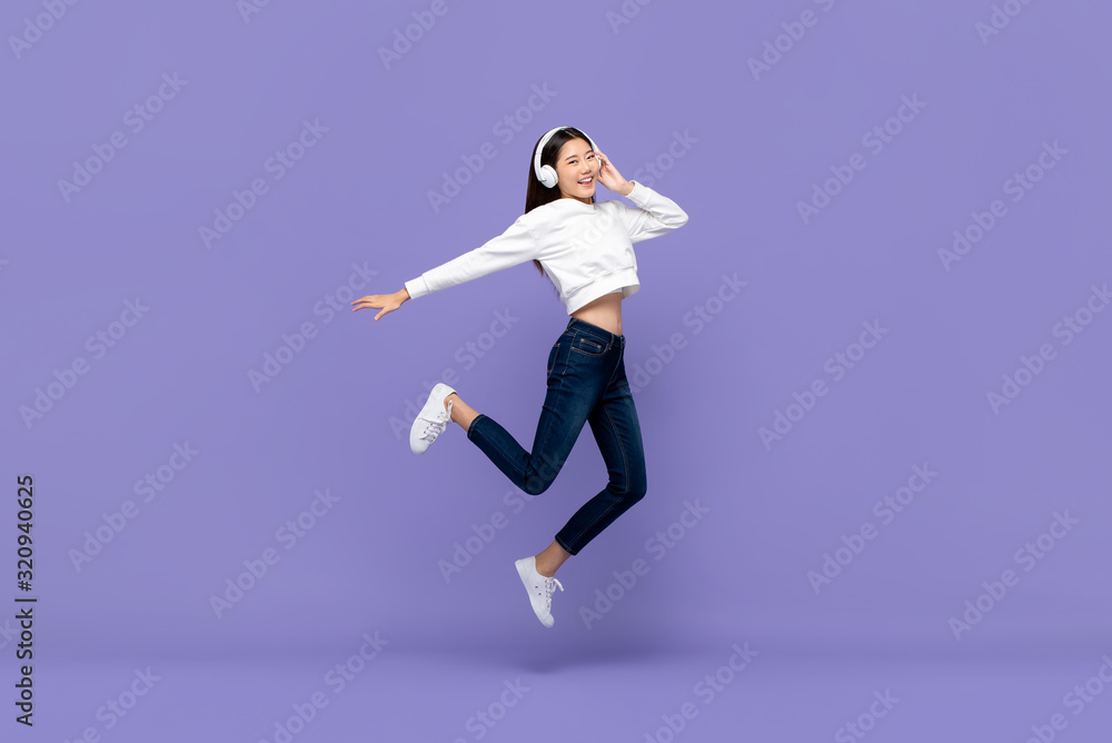 Asian woman jumping and listening to music on headphones