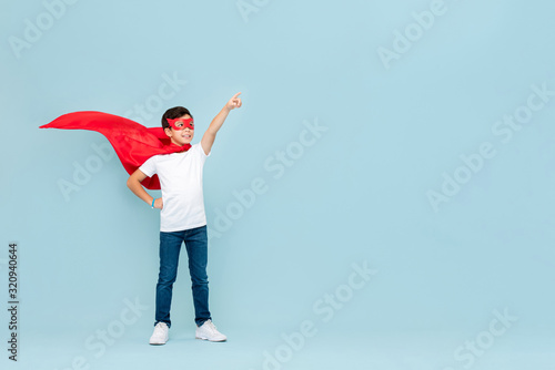 Fotografia Smiling superhero boy in red mask and cape pointing hand aside
