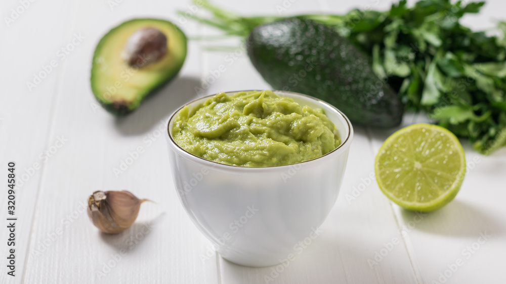 White bowl with guacamole and avocado fruit on a white wooden table. Diet vegetarian Mexican food avocado. White bowl with guacamole and avocado fruit on a white wooden table. Diet vegetarian Mexican food avocado.