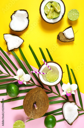Coconut summertime entertaining theme flat lay creative layout overhead with coconuts filled with summer drinks and cocktails on modern pink and yellow table top.