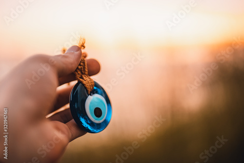 Man holding evil eye bead in his hand at sunset. photo