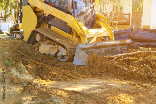 Mini bulldozer working with earth soil while doing landscaping works on construction