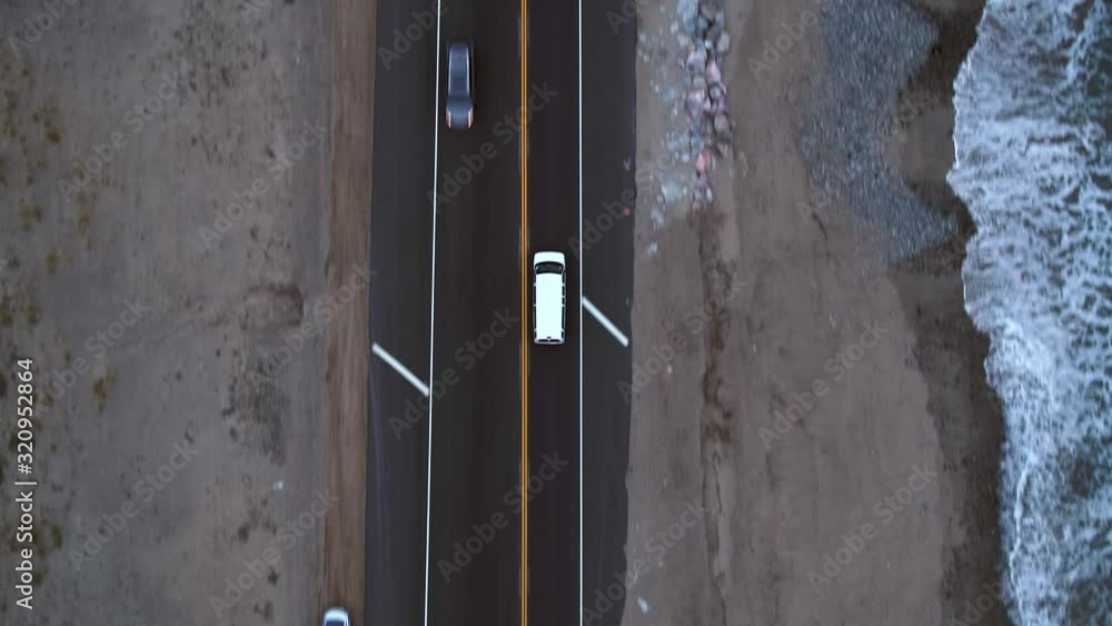 Aerial, birdseye, drone shot, following a white car on the Pacific coast highway 1, dark evening, in Los Angeles, California, United states Aerial, birdseye, drone shot, following a white car on the Pacific coast highway 1, dark evening, in Los Angeles, California, United states