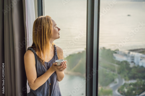 Young woman is drinking coffee in the morning on the background of a window with a sea view