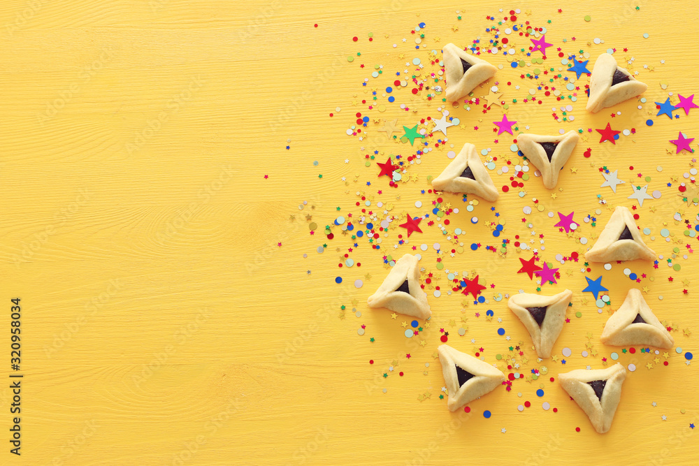 Purim celebration concept (jewish carnival holiday). Hamantaschen cookies over yellow wooden background with confetti