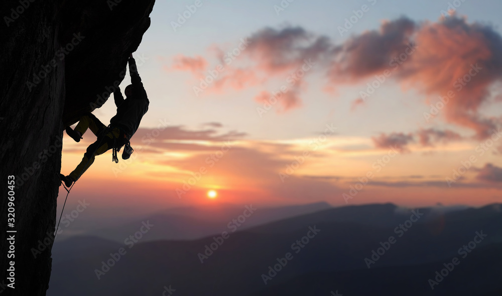 Male climber in rock climbing equipment, pulling up and doing next step on high cliff reaching rocky top. Side view. Panoramic view of mountains and amazing pink sky with sunset and clouds. Copy space - obrazy, fototapety, plakaty 