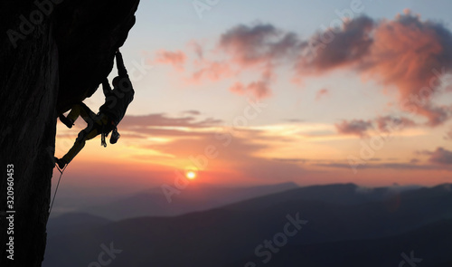 Fotografia Male climber in rock climbing equipment, pulling up and doing next step on high cliff reaching rocky top
