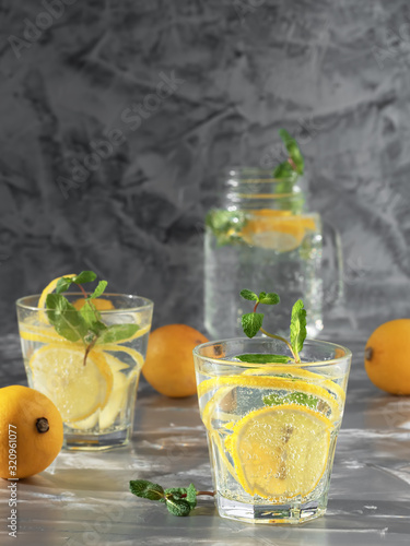 Two glass with lemonade or mojito cocktail with lemon and mint. Cold refreshing drink or beverage with ice on dark background. Copy space