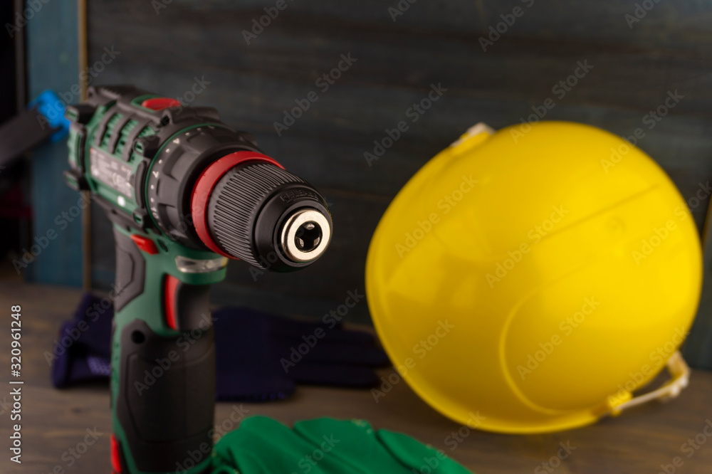 Cordless drill and yellow protective helmet Cordless drill and yellow protective helmet