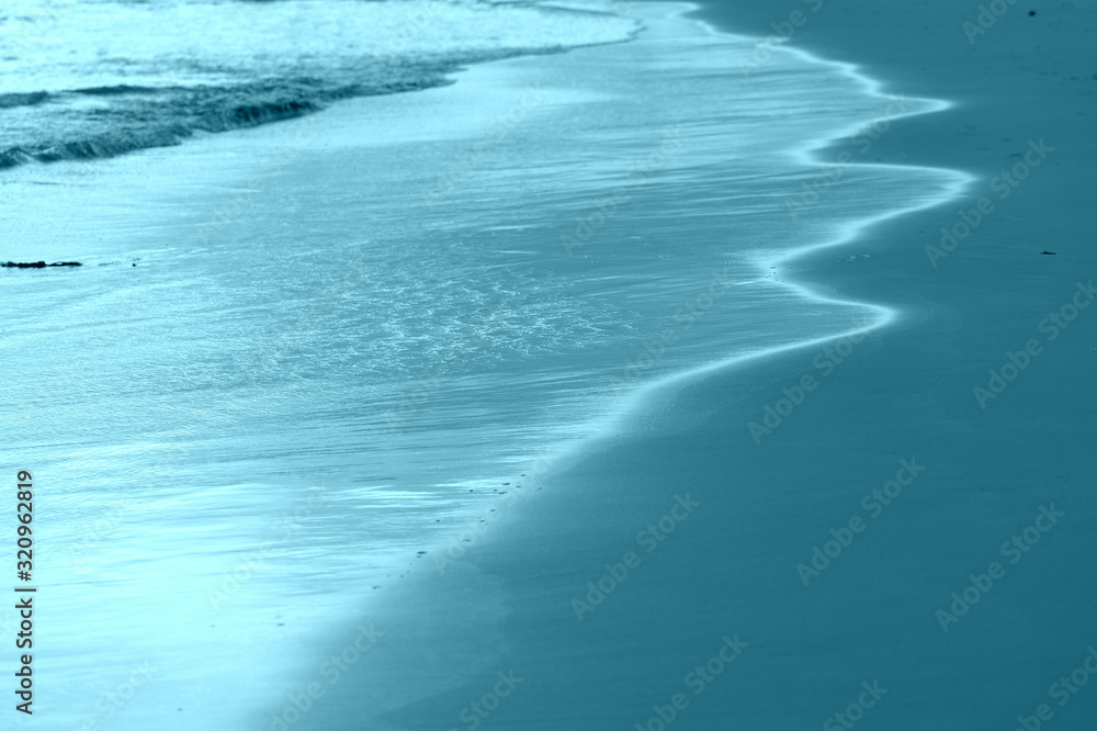 The coastal sand washed by the waves lit by the evening sun. Natural abstract background blue color toned