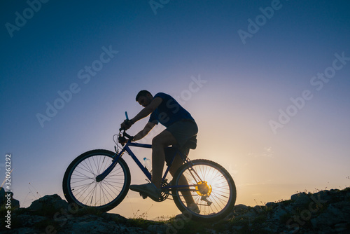 Silhouette of a fit male mountain biker riding his bike uphill on rocky harsh terrain on a sunset. © qunica.com