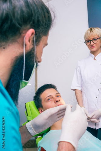 Happy teenage patient is smiling to his dentists while they are explaining him the dental treatment.