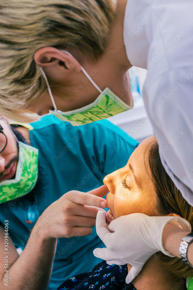 Close up portrait of a beautiful young lady sitting in the dental chair while stomatologist ( dentist ) with hands in sterile gloves is fixing her teeth. Close up portrait of a beautiful young lady sitting in the dental chair while stomatologist ( dentist ) with hands in sterile gloves is fixing her teeth.