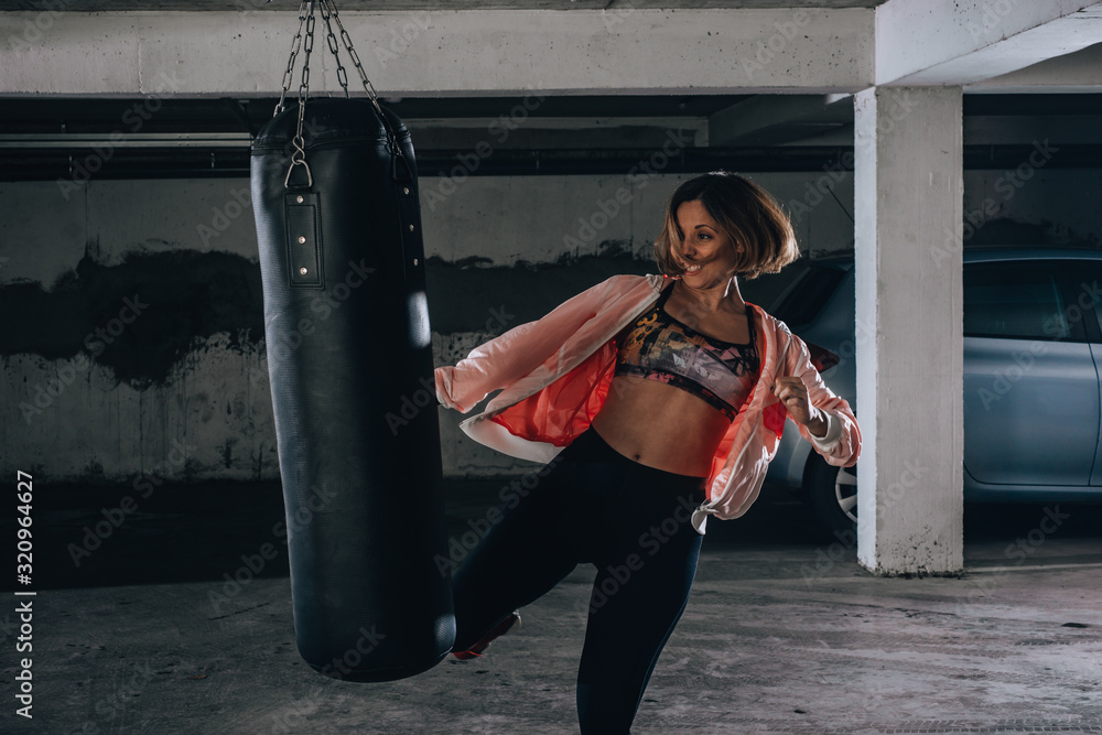 Young sportswoman doing high kick during boxing exercise in a garage.