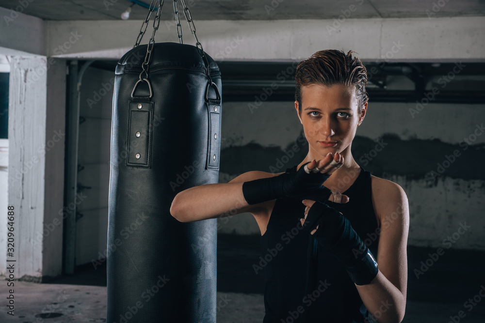Picture of focused young woman preparing her black bandages for boxing inside a garage.
