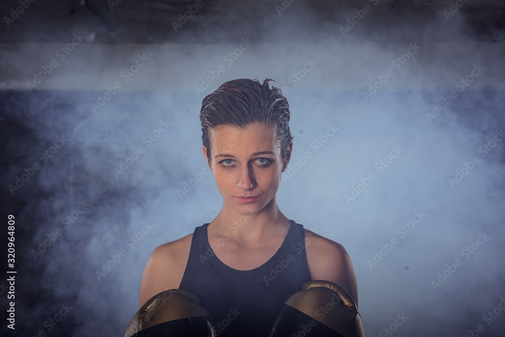 Portrait of confident young female boxer wearing boxing gloves with smoke in the background