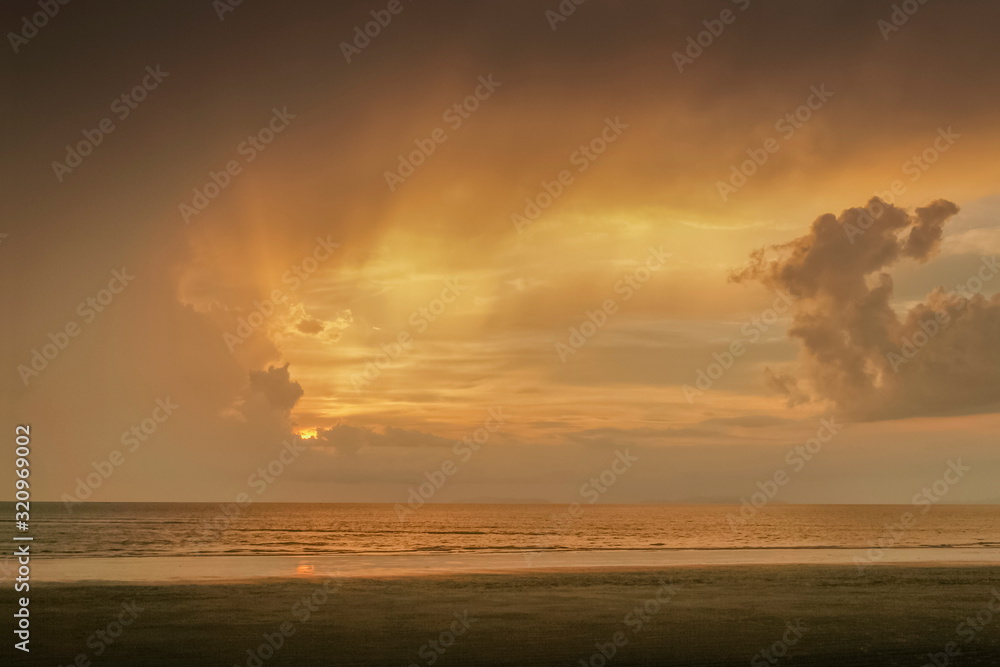 view seaside of dark clouds moving above the sea with soft rain and yellow sun light in the sky background, sunset with raining at Laem Son beach, Laem Son National Park, Ranong, southern of Thailand.