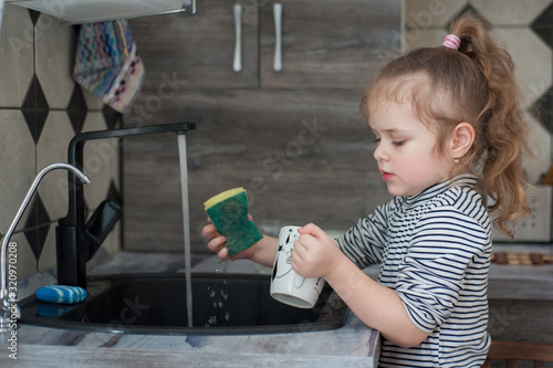Little girl washes dishes in the kitchen photo