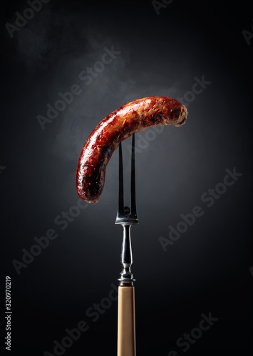 Fototapeta Grilled Bavarian sausage on a fork.