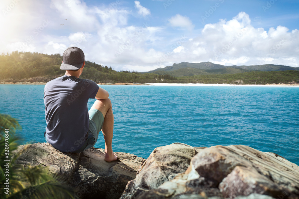 Young man sitting on a rock surrounded by tropical waters