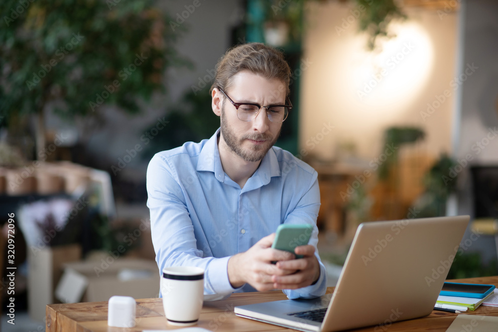 Fotografie Young man with smartphone in his hands sitting at computer.