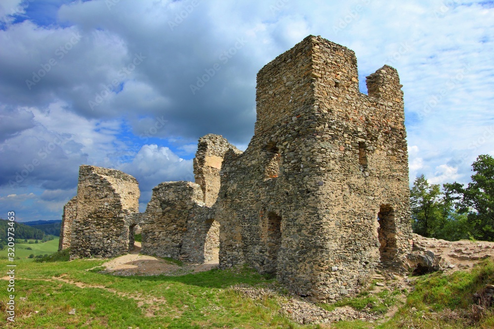 Rural stone ruins of gothic castle. Green grass, medieval castle architecture and sky with clouds. Old ruin with grass, sky and clouds. Summer outdoor trip to a ruin.