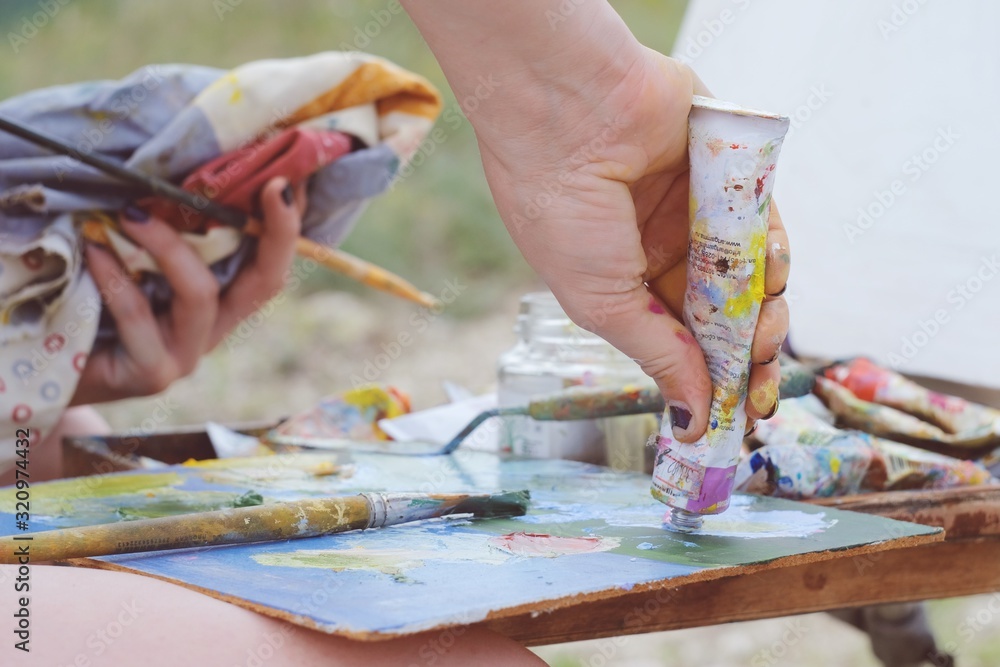 Close up view on the hands and tools of an artist. Colorful workplace of the artist with oilcan and oil paints in the plein air. Plenary session. Close up view on the hands and tools of an artist. Colorful workplace of the artist with oilcan and oil paints in the plein air. Plenary session.