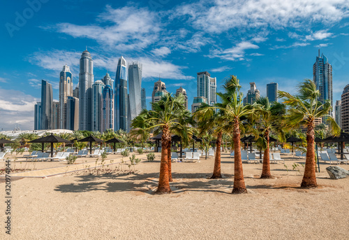 Fototapeta Naklejka Na Ścianę i Meble -  Sandy beach with palm trees against the background of Dubai Marina skyscrapers