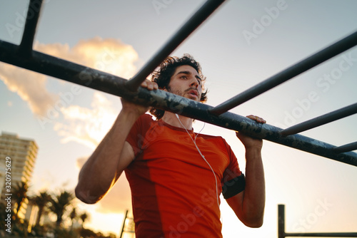 Close-up of a young male athlete doing exercises on bar in the gym park against sky - man doing pull-ups outdoors
