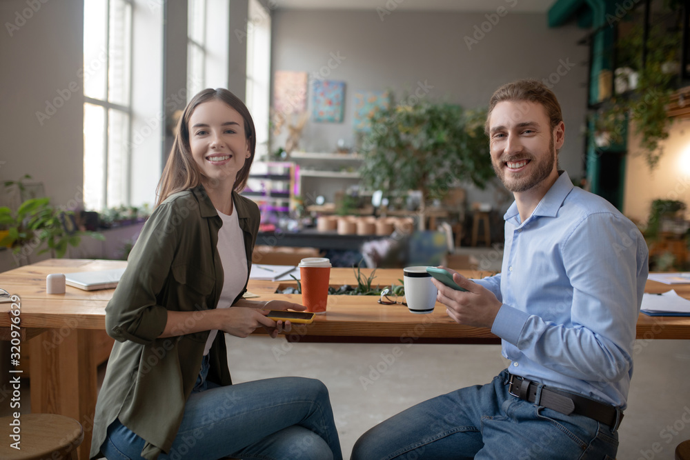 Smiling colleagues having coffee and using their smartphones together Smiling colleagues having coffee and using their smartphones together