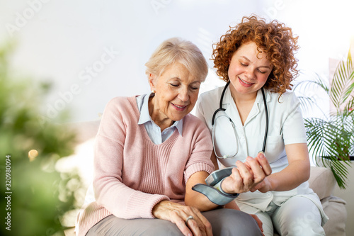 Caregiver measuring blood pressure of senior woman at home. Kind carer measuring the blood pressure of a happy elderly woman in bed in the nursing home. © Graphicroyalty