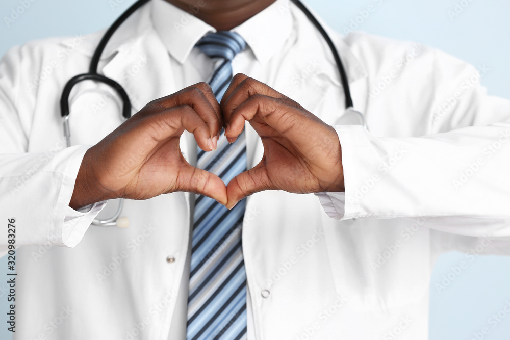 African-American doctor making heart with his hands on color background, closeup African-American doctor making heart with his hands on color background, closeup